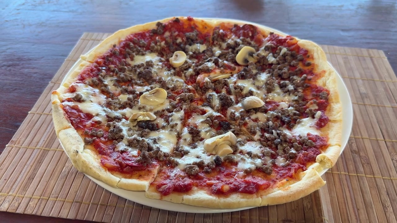 Pizza appena sfornata condita con carne macinata e funghi