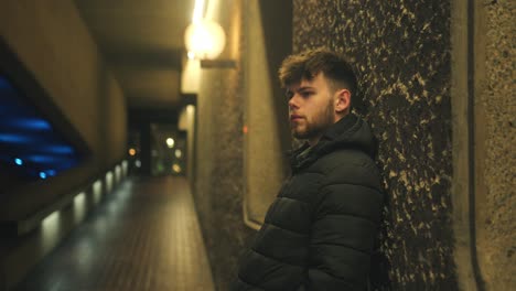 man leangs against walk in dimly lit barbican corridor, dark atmosphere with strong shadows and brutalist detail