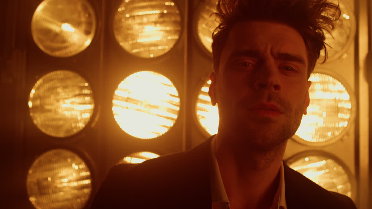 남자 모델이 나이트 클럽의 조명을 가까이 돌리고 있다. 남자가 자신있게 서 있다.