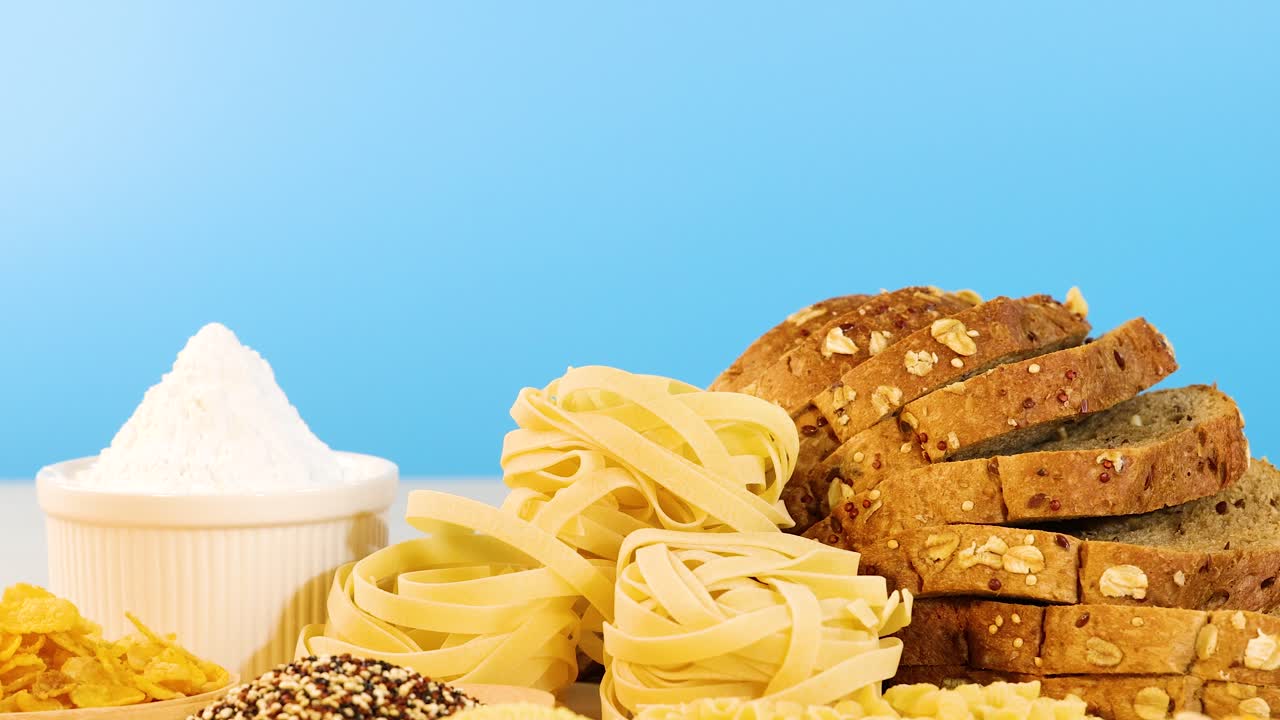 Various grains, breads, and pasta arranged against a bright blue backdrop. Static composition with vibrant lighting and clear focus