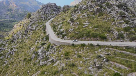 Toma-Panorámica-De-Montañas-Con-Un-Camino-Sinuoso-Siguiendo-A-Un-Auto-Bajando-En-Sa-Calobra,-Mallorca,-España