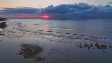 rising drone clip showing beach shoreline and pink sunset reflecting on the calm open ocean in bali, indonesia