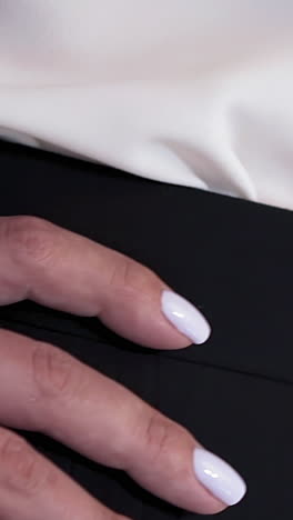 elegant woman wearing black skirt and silk blouse holds hand with stylish white manicure on waist posing for camera closeup slow motion