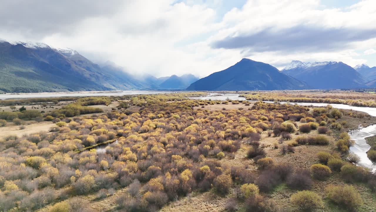 Aerial view of Glenorchy's vast landscape with mountains, vibrant foliage, and a winding river under cloudy skies