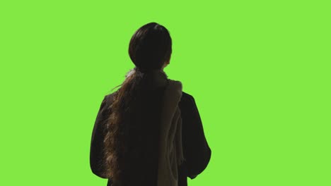 rear view low key studio shot of woman looking all around frame against green screen in vr environment