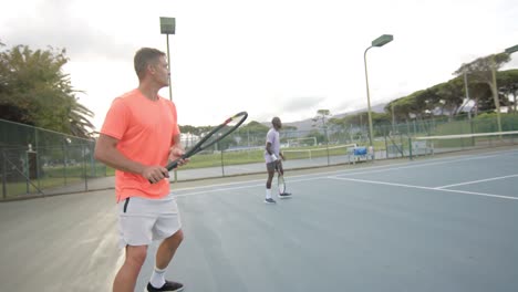 two diverse male friends playing doubles returning ball on outdoor tennis court in slow motion