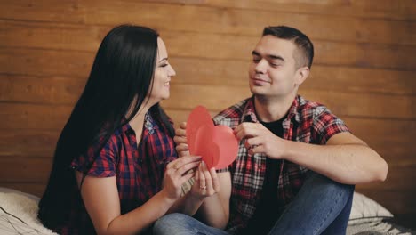 beautiful couple are laying out in their hands red paper hearts of large and small sizes on the background of a wooden wall in the studio. love story. valentine's day