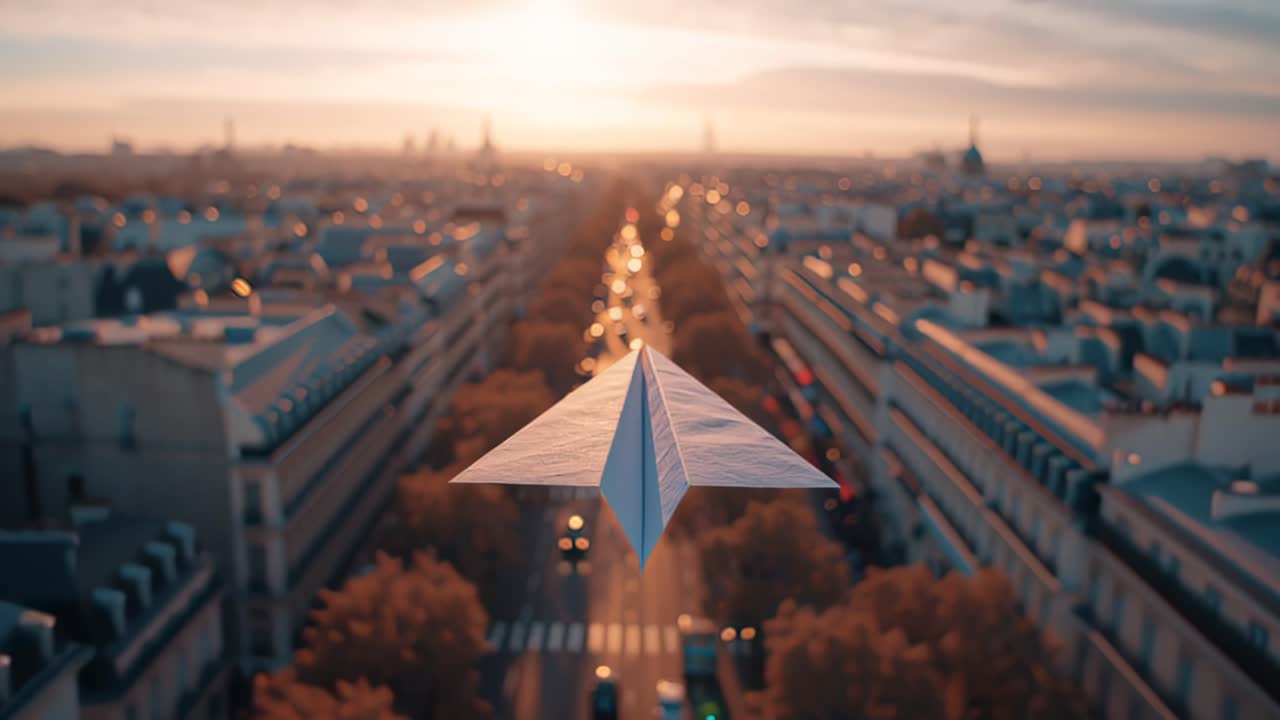 Metraje cinematográfico de un avión de papel blanco deslizándose sobre una larga calle de la ciudad durante la hora dorada, con suaves luces de tráfico bokeh y tejados de fondo.