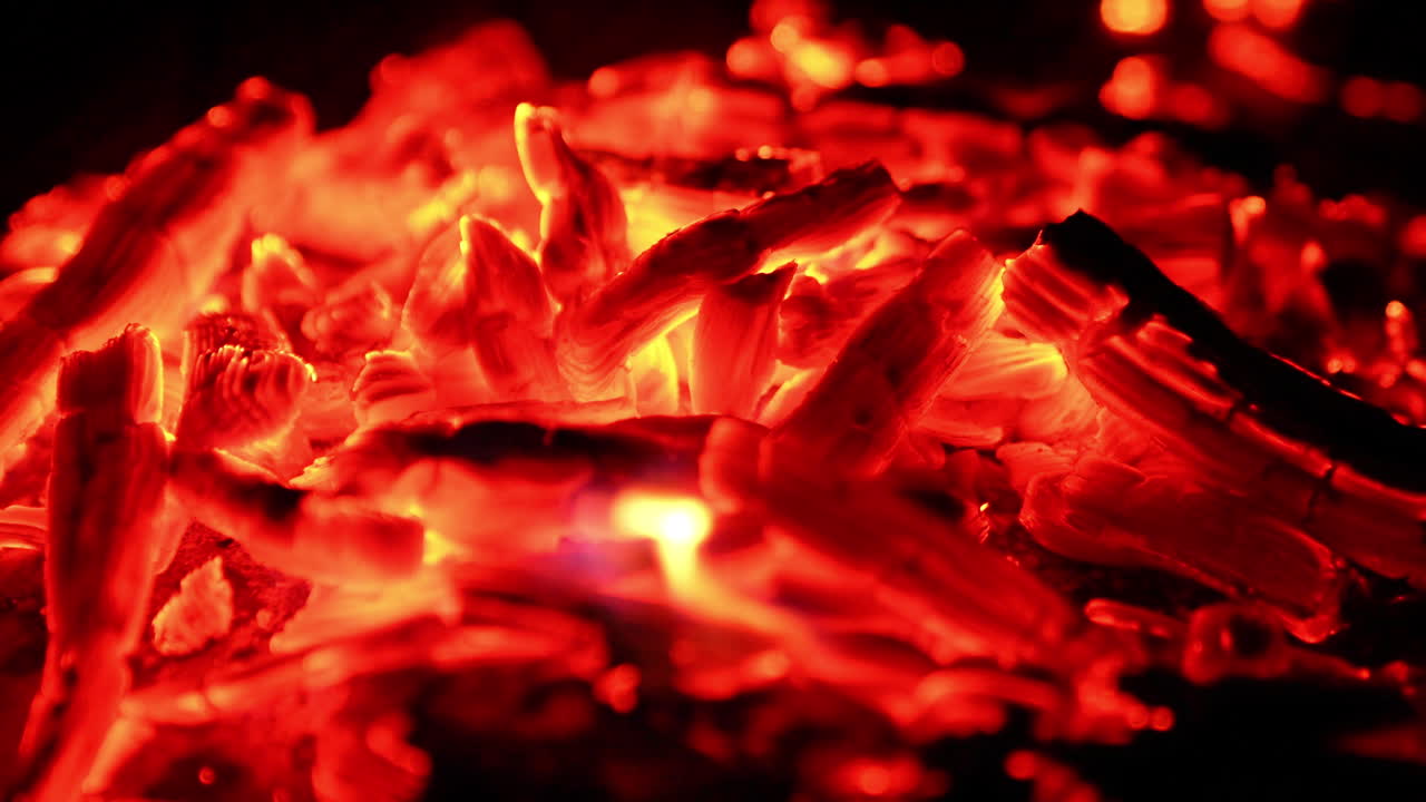 Sparkling pieces of embers in the pile. Close view of the burnt out wood smoldering at dark backdrop.