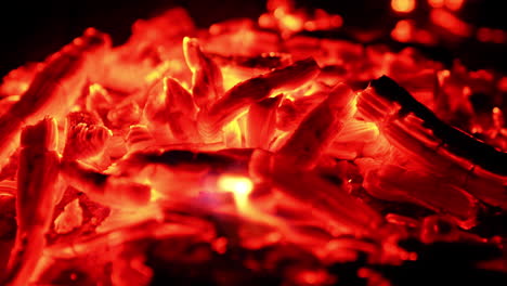sparkling pieces of embers in the pile. close view of the burnt out wood smoldering at dark backdrop.