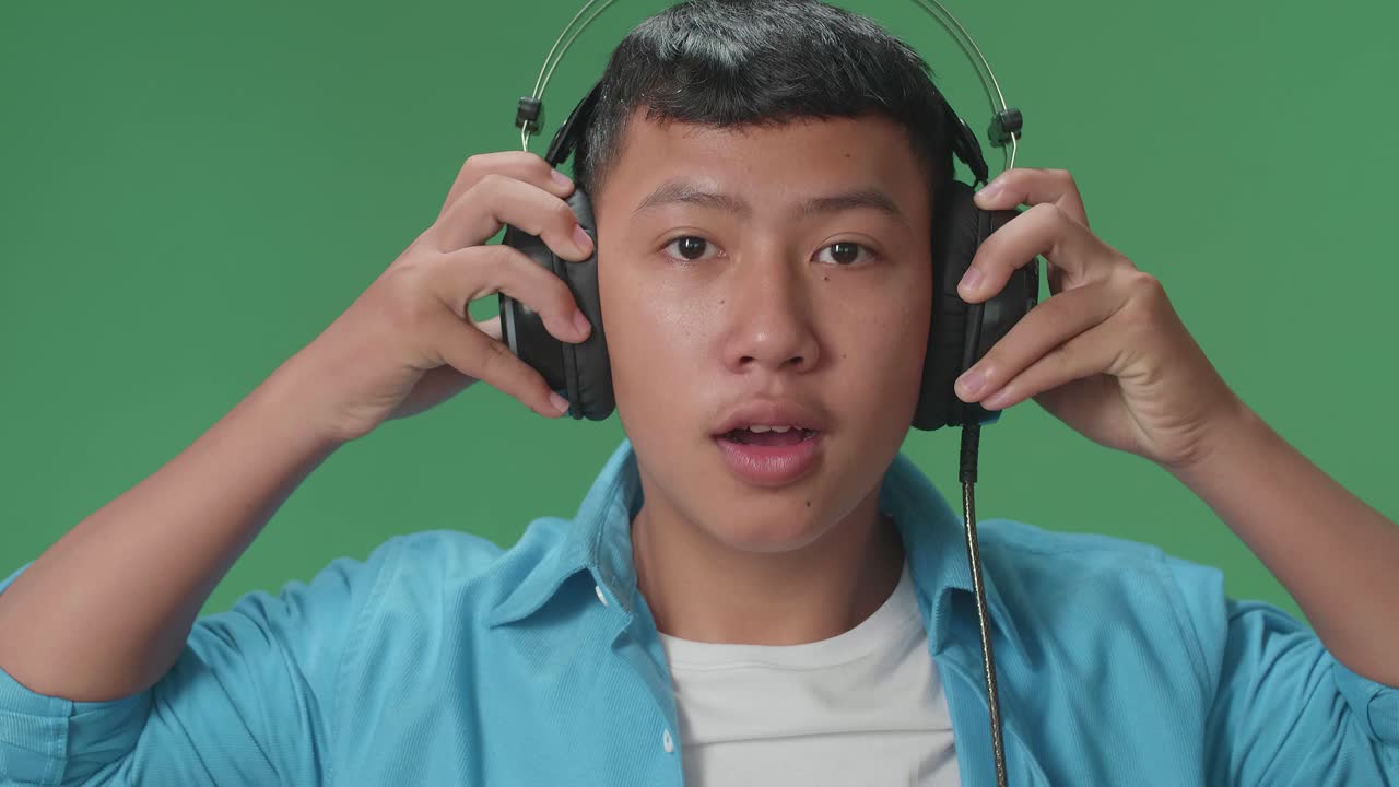Young Asian Boy Listening To Music With Headphones And Dancing In The Green Screen Studio