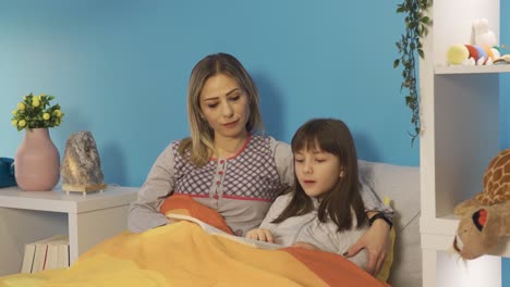 la niña está leyendo un libro con su madre antes de irse a dormir.