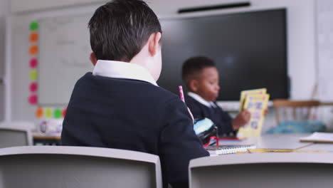 Back-view-of-boy-with-Down-Syndrome-sitting-at-desk-drawing-in-a-primary-school-lesson,-close-up