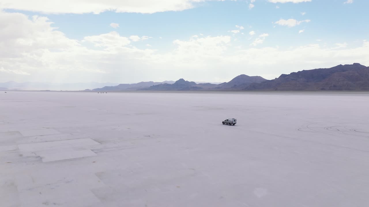 Low aerial ascends above truck campervan driving along Bonneville Salt Flats Utah