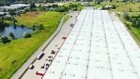 Toma-Aérea-De-Un-Camión-Con-Un-Semirremolque-Adjunto-Que-Sale-Del-área-De-Carga-Del-Edificio-De-Almacenamiento-Industrial-Donde-Muchos-Camiones-Están-Cargando-Y-Descargando-Mercancías