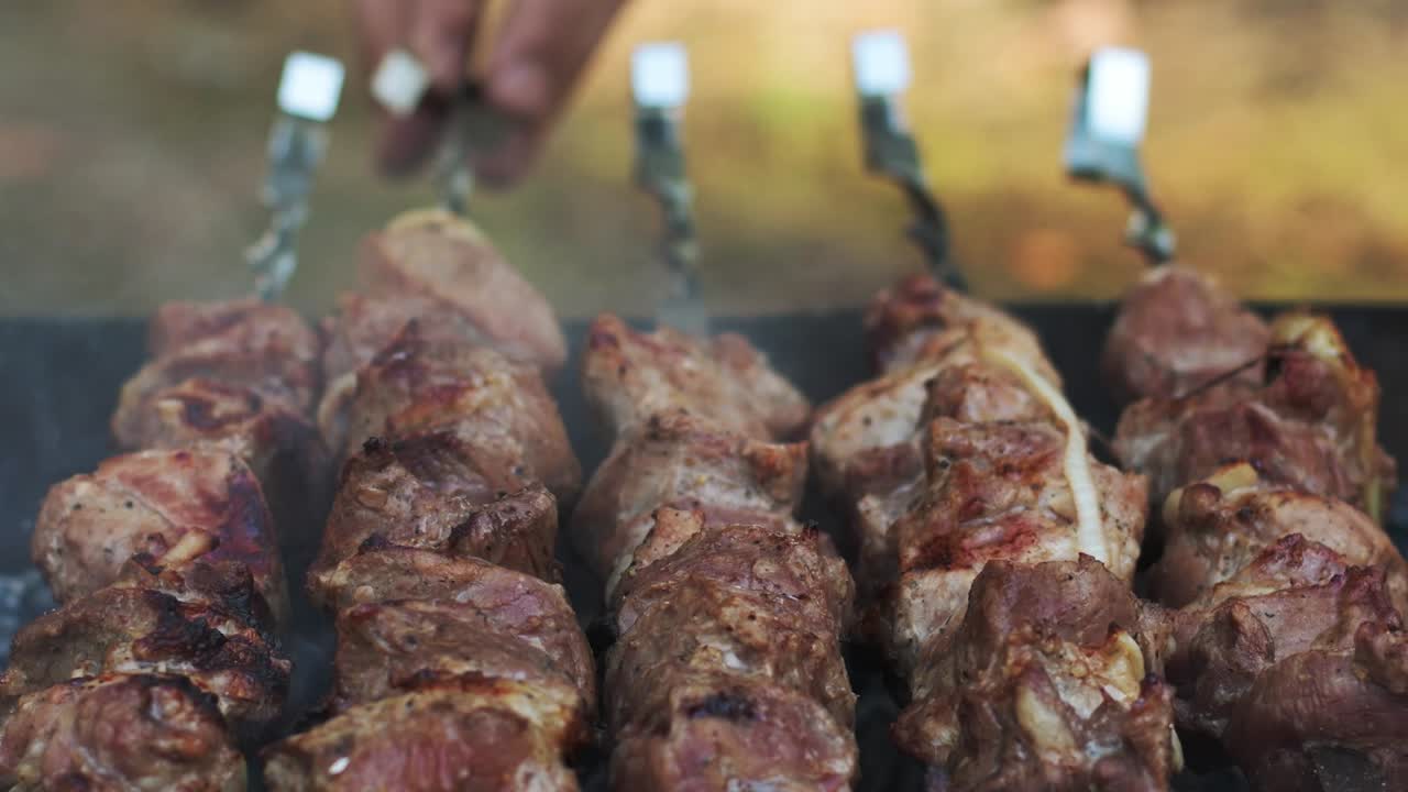 Carne per barbecue che griglia su una griglia aperta all'aperto. Primo piano della mano di un uomo che gira gli spiedini di carne.