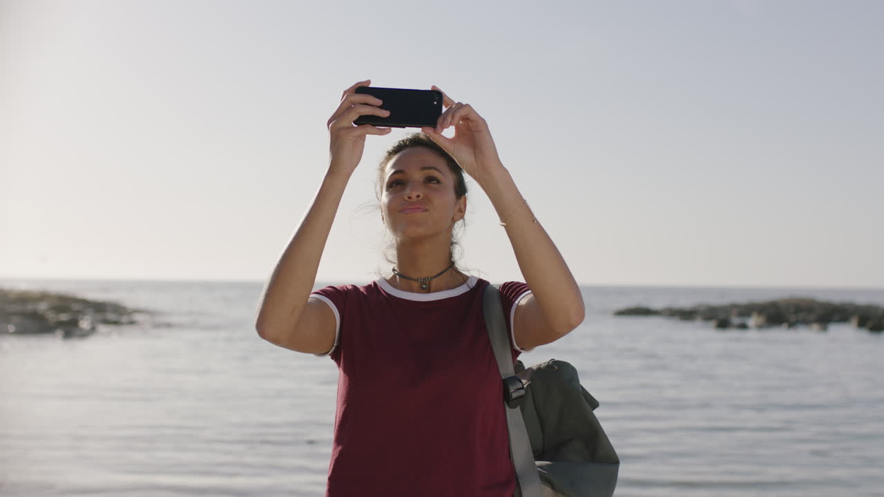 retrato de una joven mujer hispana tomando fotos en la playa usando un teléfono inteligente disfrutando de un relajado día soleado