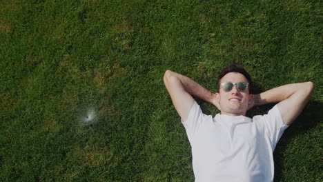 a young man lies under jets of water from automatic irrigation, escapes from the heat