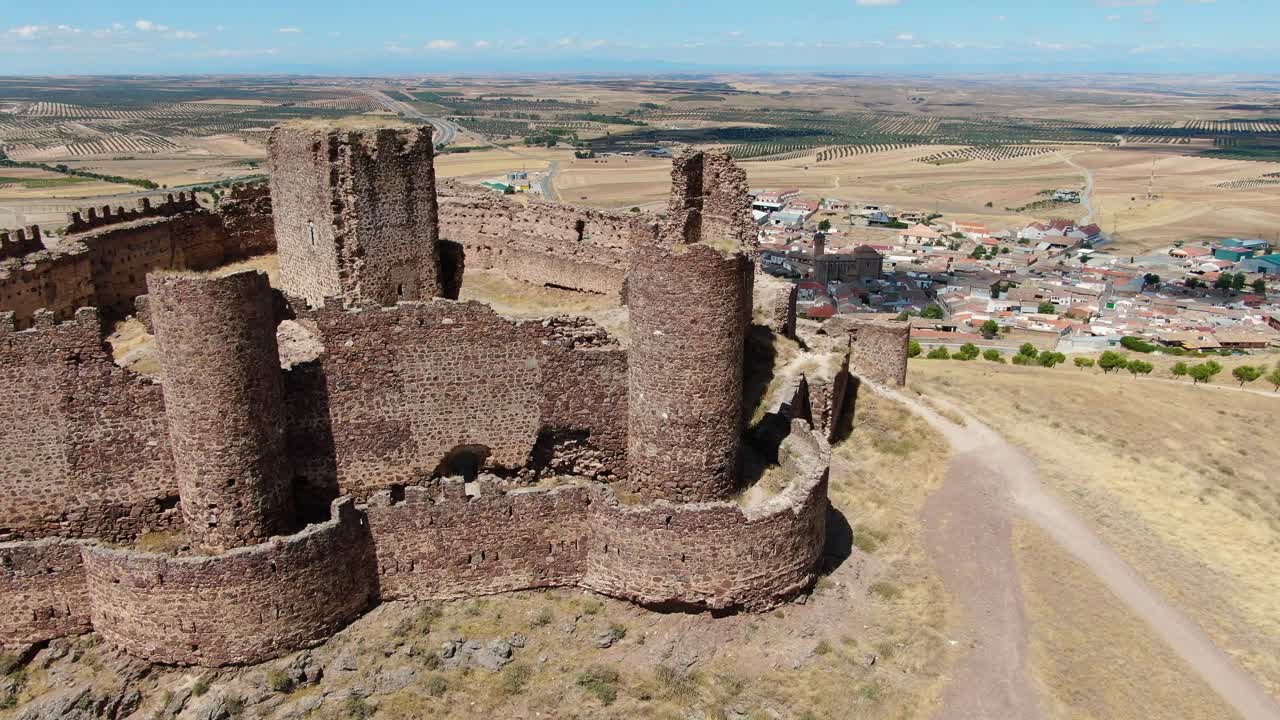 vuelo lateral con un dron visualizando una fortaleza amurallada en ruinas ubicada en una colina y dando paso a una ciudad rodeada de tierras de cultivo en un día de verano con un cielo azul con nubes en toledo, españa