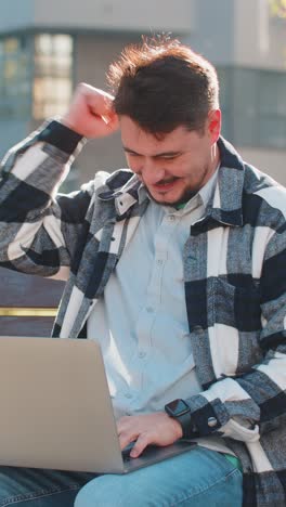 overjoyed happy mature man working on laptop netbook screaming in delight on bench in downtown city