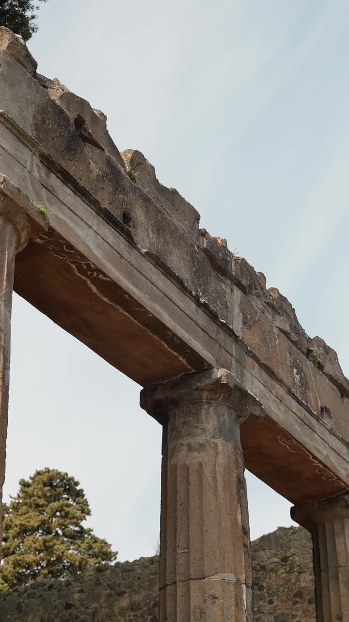 Antico colonnato a Pompei, Italia, che si erge contro il cielo con colonne romane logorate dalle intemperie e architravi in pietra in una scena di patrimonio archeologico verticale