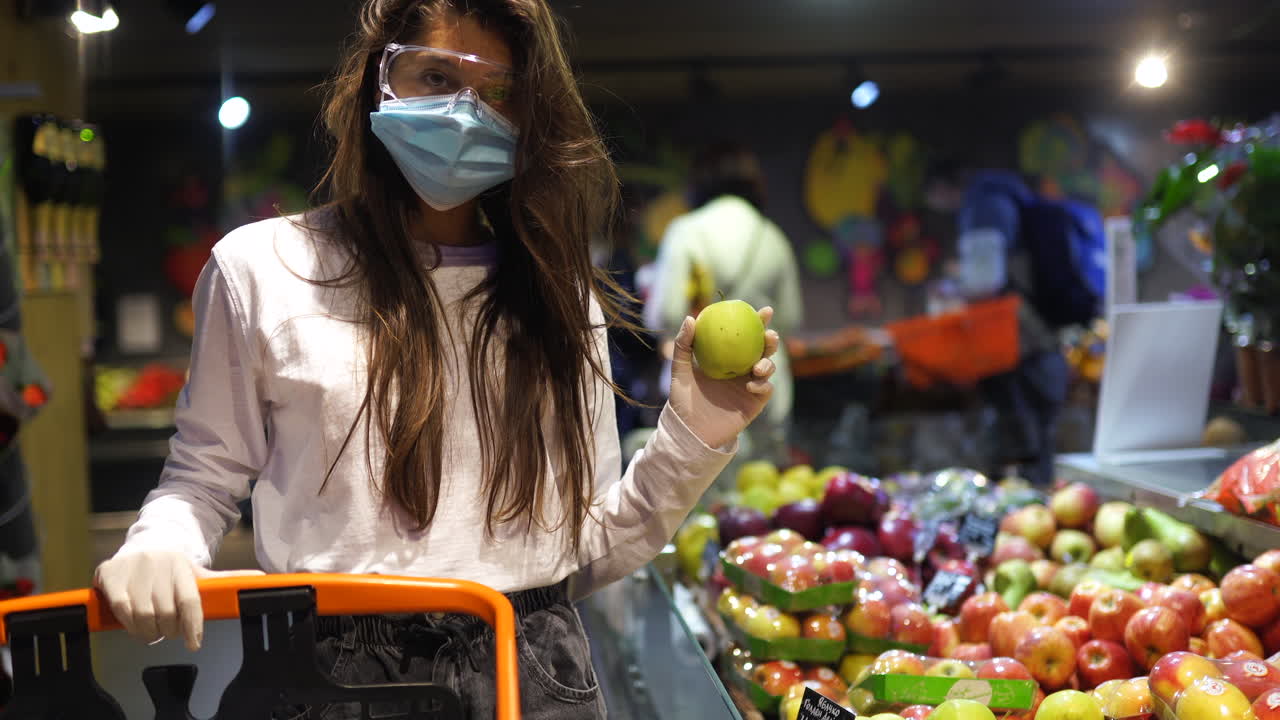 mujer comprando manzanas en una tienda de comestibles durante una pandemia
