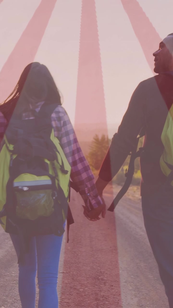 Vertical video: Sunset urging couple walking dirt road, pink sunburst showing packs for travel ad