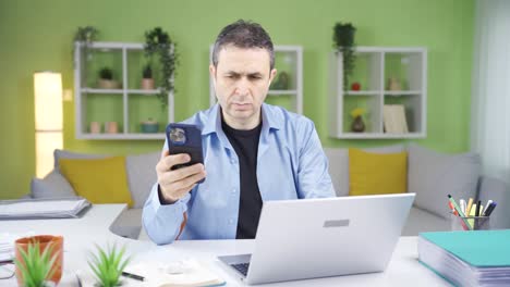 Trabajador-De-Oficina-En-Casa-Mirando-El-Teléfono-Y-Usando-Una-Computadora-Portátil-Al-Mismo-Tiempo.