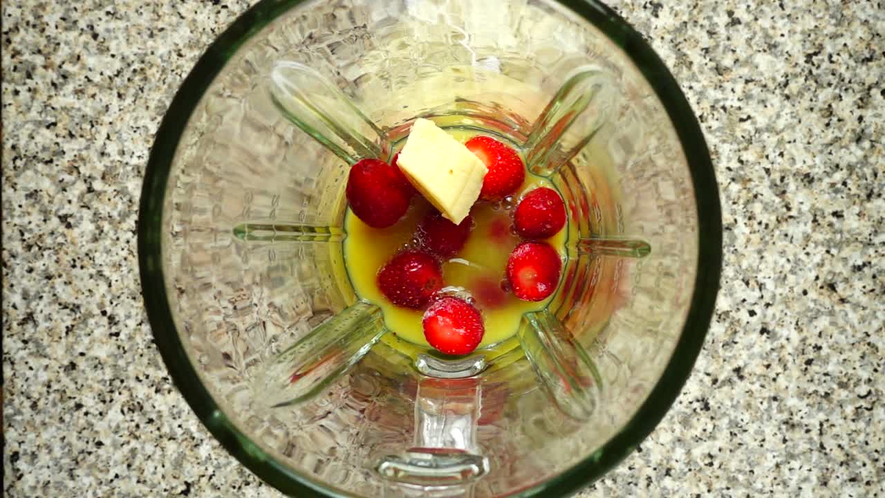 Pieces of bananas fall on strawberry in orange juice. Slow motion. Shooting in kitchen. Top view