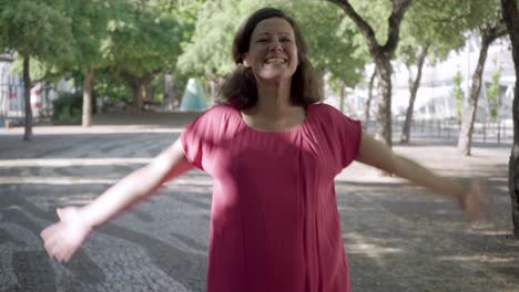 mujer madura feliz con blusa rosa posando en un parque soleado