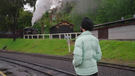View-Behind-An-Indian-Punjabi-Sikh-Man-Staring-At-Steam-Train-From-Open-Platform-On-A-Rainy-Day