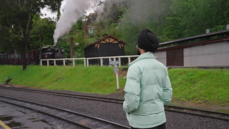 view behind an indian punjabi sikh man staring at steam train from open platform on a rainy day