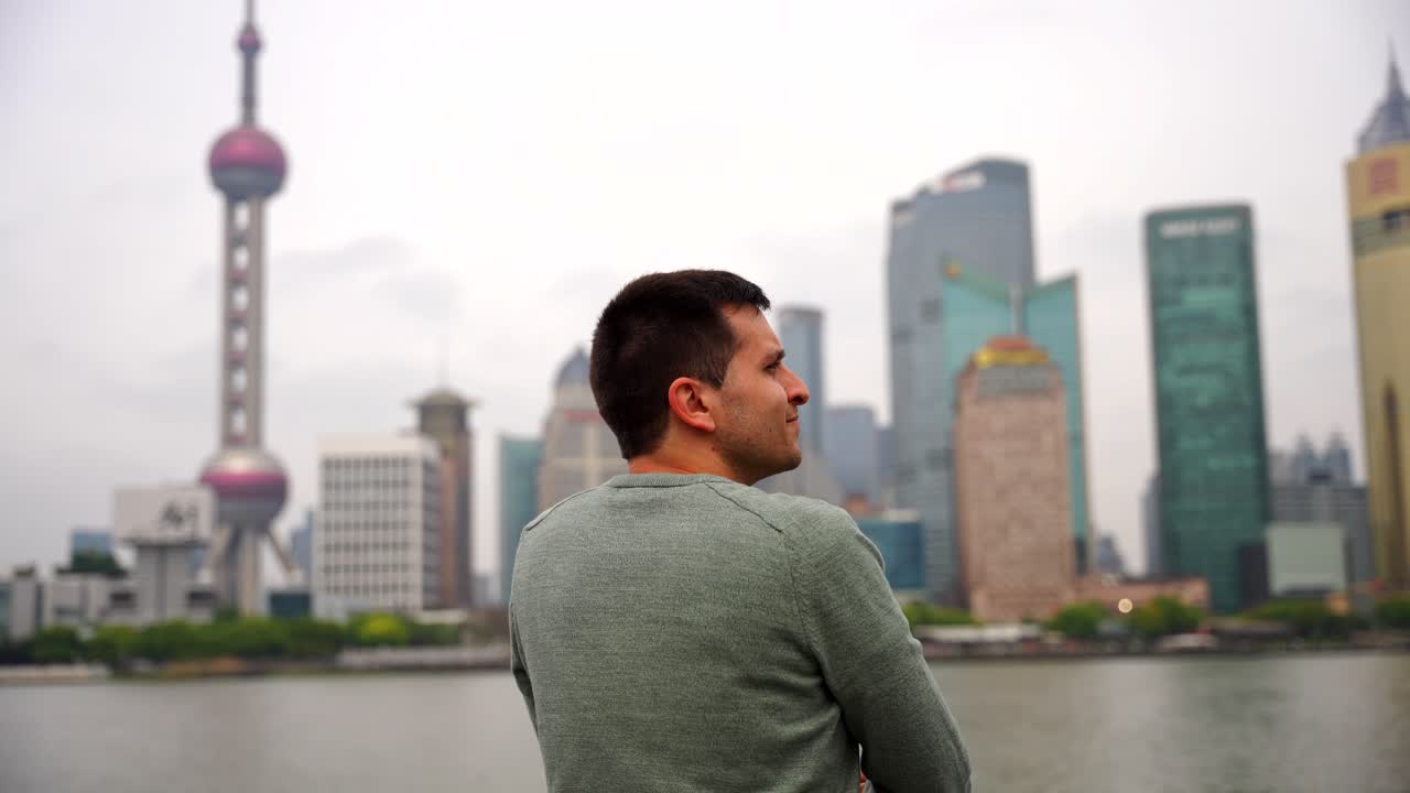 hombre caucásico con vistas al horizonte de shanghai desde la orilla del río con la torre de la perla oriental en un día nublado