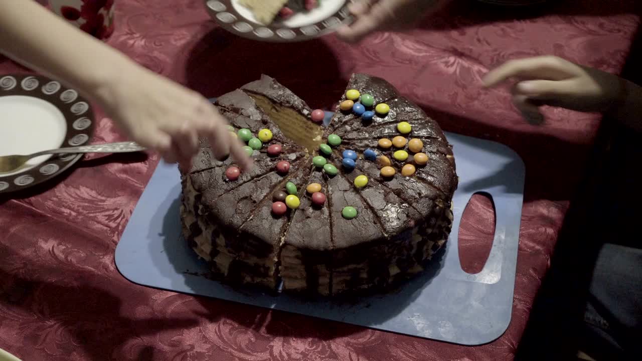 una mujer coloca en platos pedazos de pastel de chocolate cortado, decorado con dulces en la parte superior y los trata a los niños. celebración familiar. de cerca. la vista desde la parte superior. 4k.