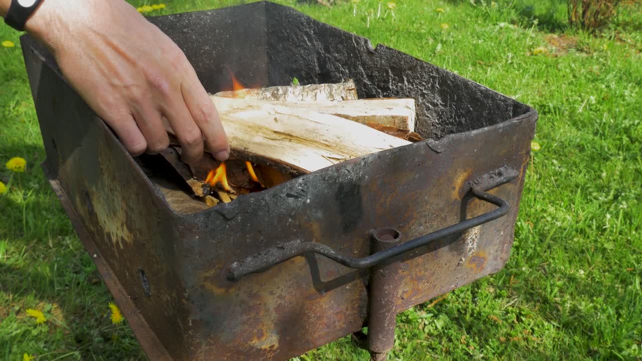 Young man laying down wood log and prepares rusty grill for baking and BBQ, medium close up shot