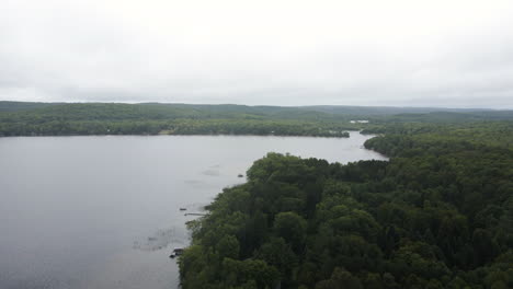 Rain-cloud-filled-sky-above-dense-forested-maple-lake-ontario,-aerial-dolly