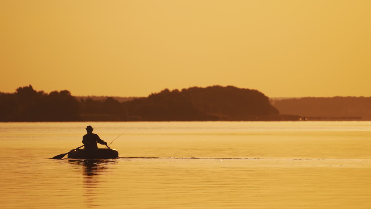 Silhouette of man sailing with two wooden oars on a small boat at sunset time. Beautiful sunset in the river and the silhouette of a man who tries to find a place for fishing on rowboat.