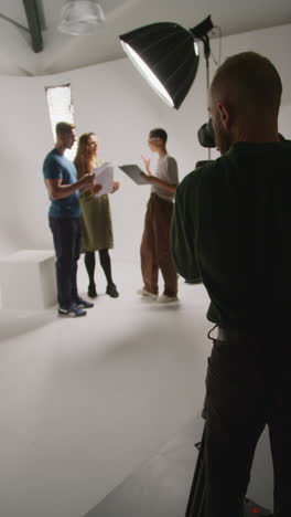 vertical video of film camera operator shooting director talking with male and female actors holding scripts rehearsing for shooting movie or video in studio 1