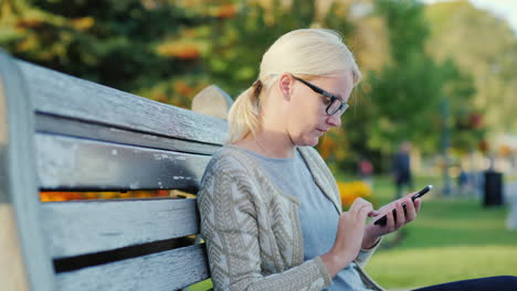 Blonde-Frau-Auf-Einer-Bank-Mit-Smartphone