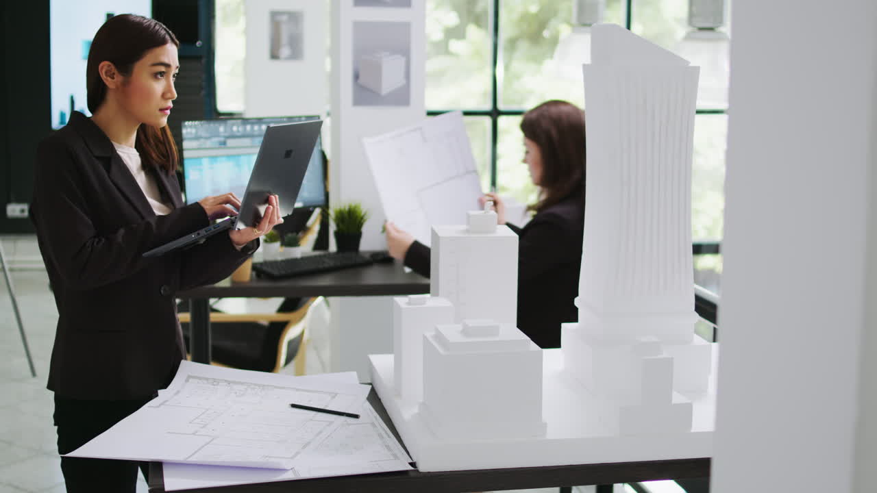 아시아 계약자는 노트북에서 3d 인쇄 모델에 대한 메모를 취합니다.