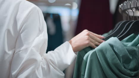 close-up of woman browsing through clothing rack, touching and observing various shades of colorful garments, focus on hand gently interacting with clothes