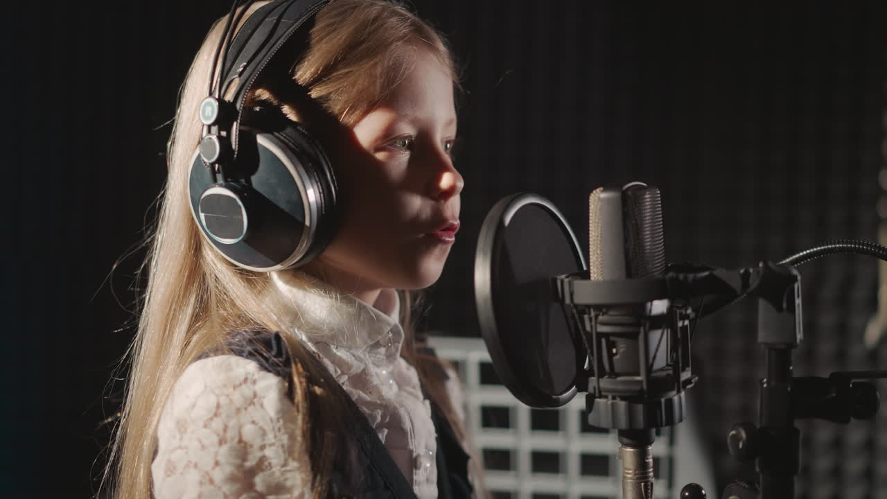 niño canta una canción en un estudio de grabación de audio. una niña linda con auriculares canta en un micrófono con filtro en una habitación aislada de sonido. niño talentoso