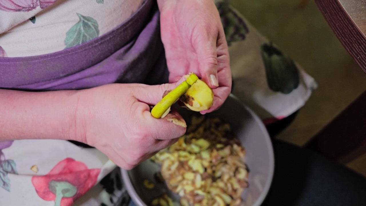 La nonna sbuccia con cura una patata fresca a mano, preparazione di un pasto fatto in casa.