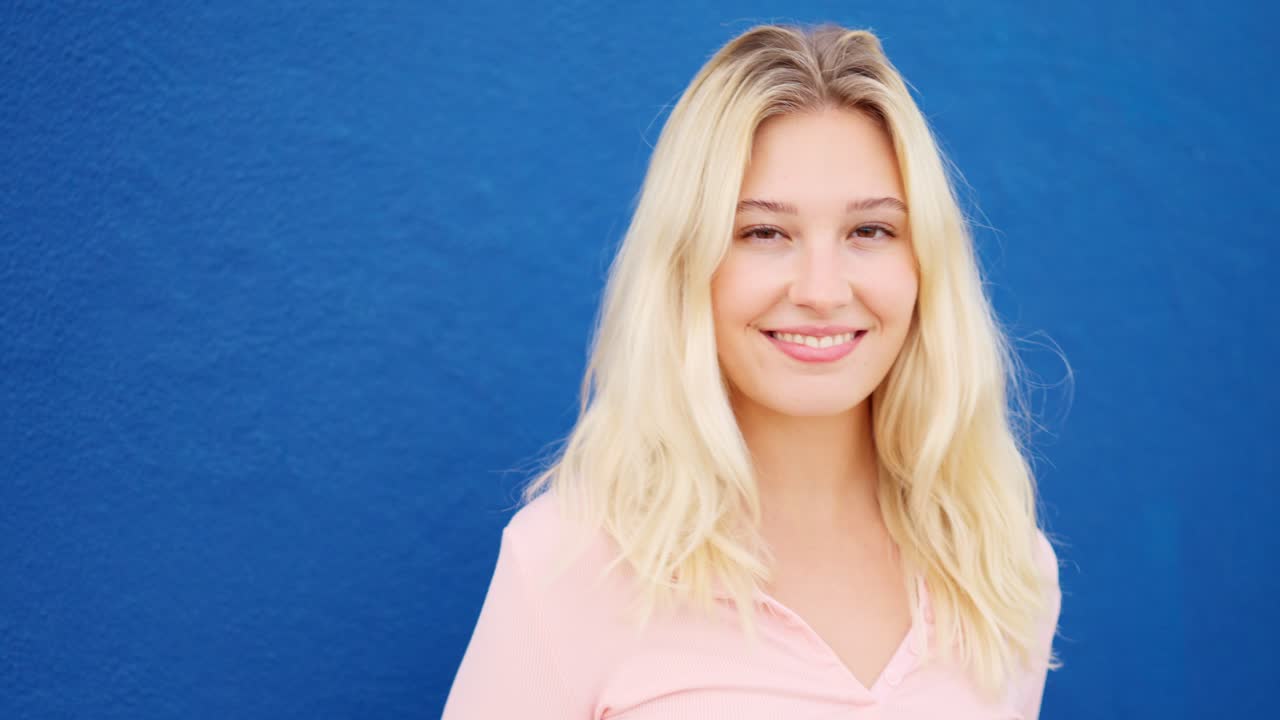 Blonde woman smiling at camera next to a blue wall