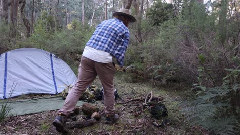 a bushman chucking firewood on a fire out in the bush