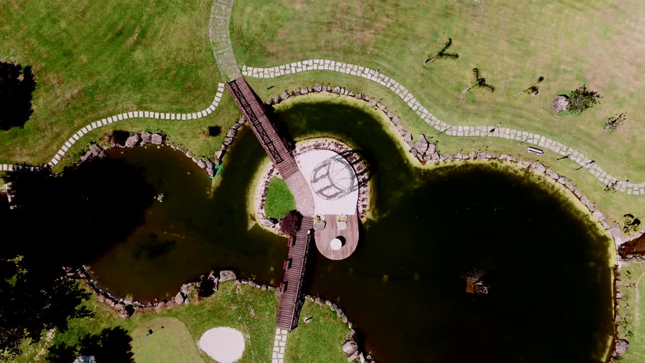 Aerial view of a serene lake with a wooden bridge and pathways on a large golf course