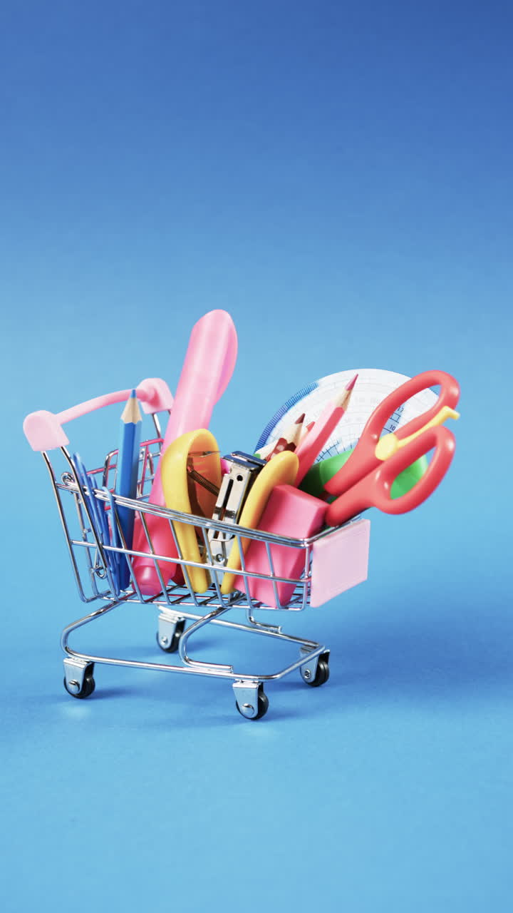 Vertical video of close up of shopping trolley with school items and copy space on blue background