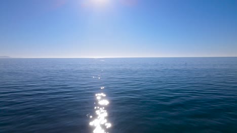 aerial dolly over rocky coast and sandy beach moving towards glimmering sunlight