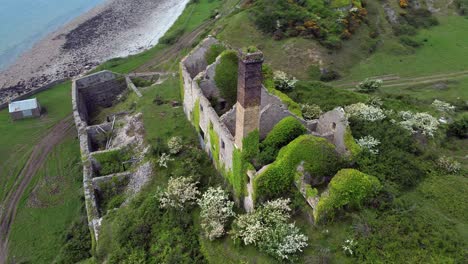 abandoned overgrown ivy covered desolate countryside historical welsh coastal brick factory mill aerial view close orbit left