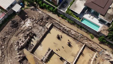 aerial view of construction site with workers building foundation in muddy pit